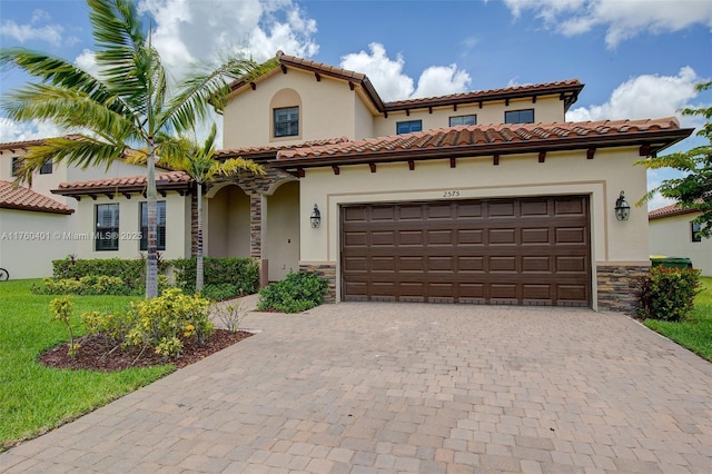 mediterranean / spanish-style home featuring stucco siding, stone siding, an attached garage, and decorative driveway