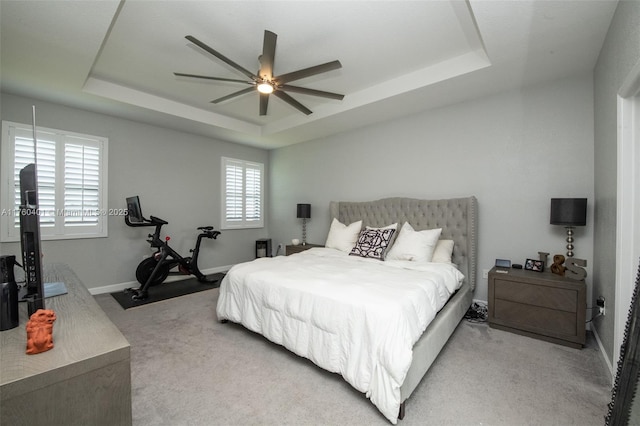 bedroom featuring light carpet, ceiling fan, baseboards, and a tray ceiling