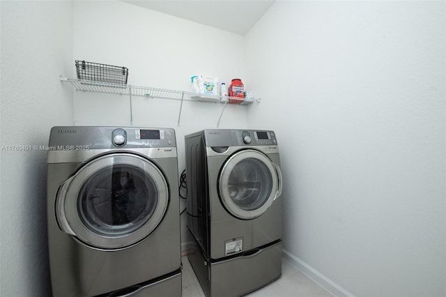 washroom with light tile patterned floors, laundry area, washing machine and dryer, and baseboards