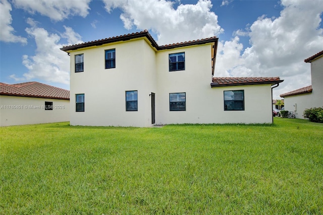 back of property featuring a yard, stucco siding, and a tile roof