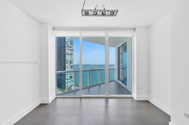 empty room featuring baseboards, a textured ceiling, floor to ceiling windows, and a water view