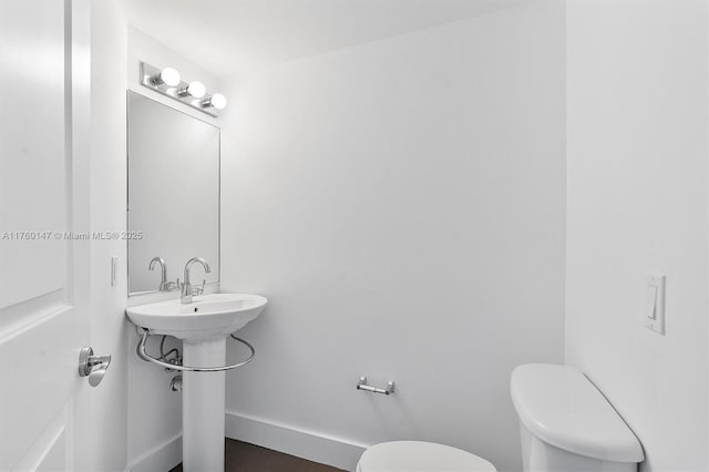 half bathroom featuring a sink, baseboards, and toilet