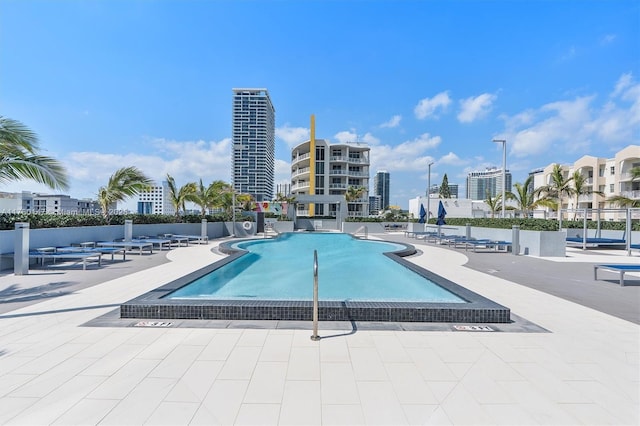 community pool with a patio area, a view of city, and fence