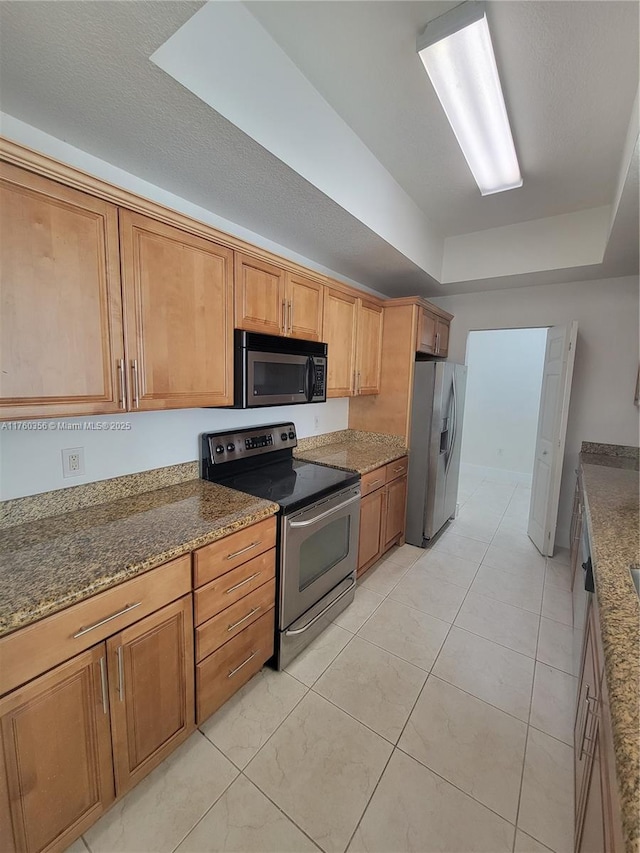 kitchen with light tile patterned floors, appliances with stainless steel finishes, stone countertops, and a tray ceiling