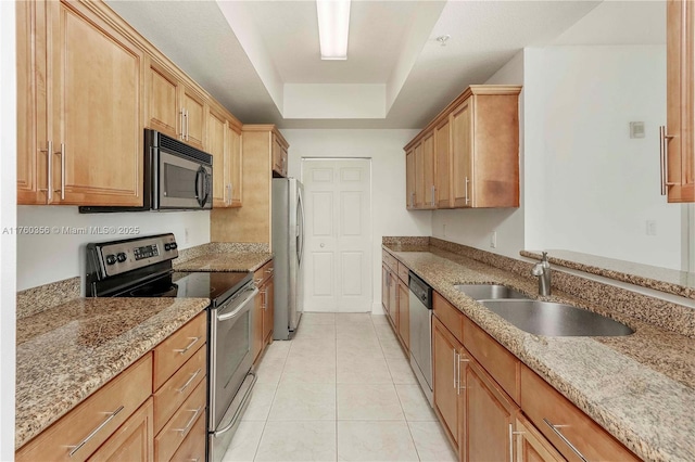 kitchen with appliances with stainless steel finishes, a sink, light stone counters, a tray ceiling, and light tile patterned flooring