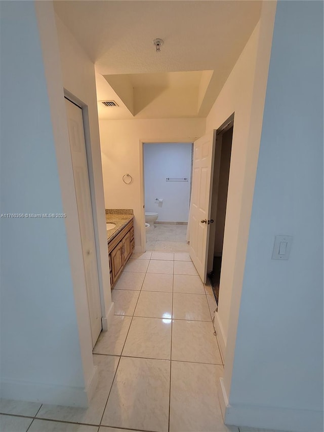 hall featuring light tile patterned floors, baseboards, and visible vents