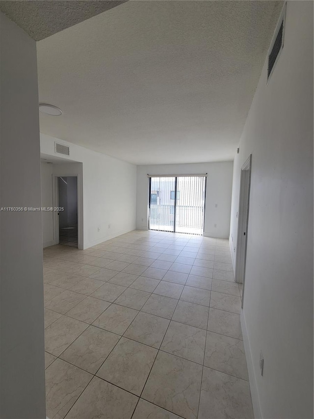 spare room featuring light tile patterned floors, visible vents, a textured ceiling, and baseboards