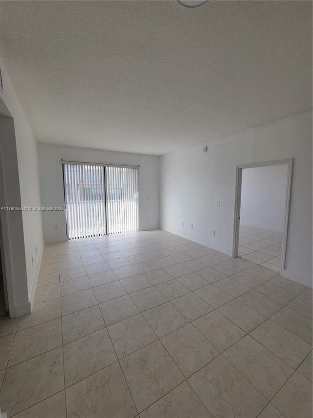 unfurnished room with light tile patterned flooring, baseboards, and a textured ceiling