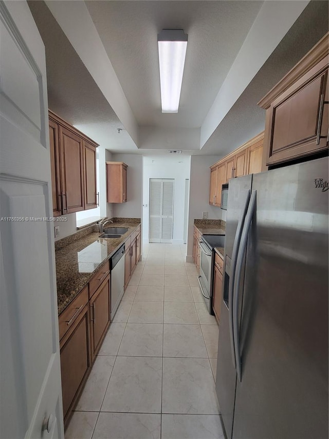 kitchen with visible vents, dark stone counters, light tile patterned flooring, stainless steel appliances, and a sink