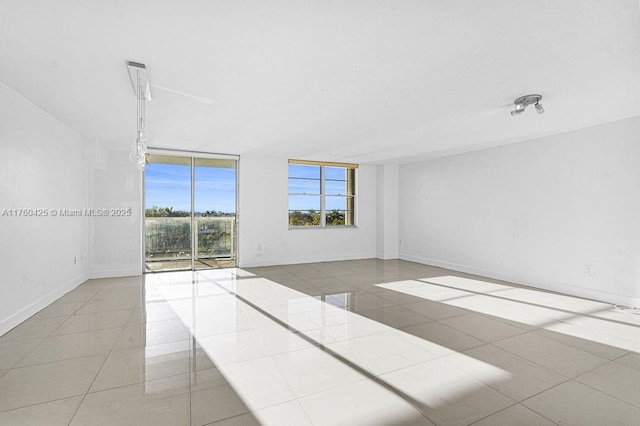 tiled empty room featuring a wall of windows and baseboards