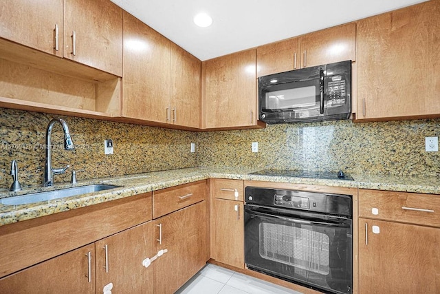 kitchen featuring a sink, light stone counters, backsplash, and black appliances