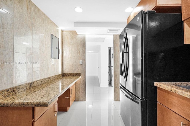 kitchen featuring tile walls, light tile patterned floors, brown cabinetry, and freestanding refrigerator