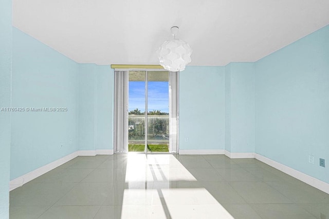 tiled empty room with a chandelier, baseboards, and expansive windows