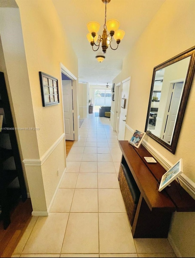 corridor with an inviting chandelier, light tile patterned floors, and baseboards