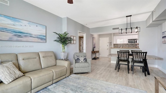 living area with visible vents, baseboards, light wood-style flooring, and a chandelier