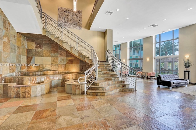 stairway with a high ceiling, expansive windows, visible vents, and stone tile flooring