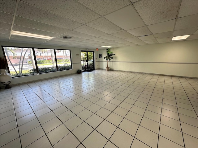 unfurnished room featuring light tile patterned floors, baseboards, visible vents, and a drop ceiling