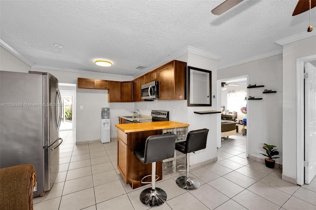 kitchen featuring light tile patterned floors, appliances with stainless steel finishes, ceiling fan, and ornamental molding