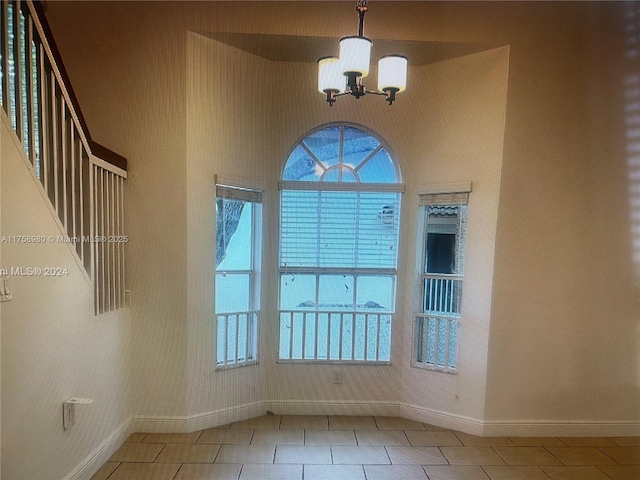 tiled spare room with baseboards, a notable chandelier, and a high ceiling