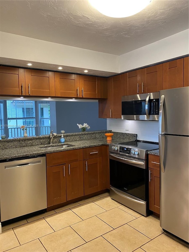 kitchen with dark stone counters, light tile patterned floors, stainless steel appliances, a textured ceiling, and a sink