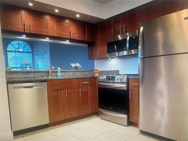 kitchen featuring tasteful backsplash, light tile patterned floors, dark stone countertops, stainless steel appliances, and a sink