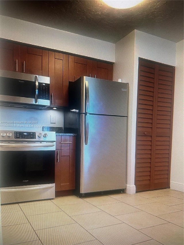 kitchen with light tile patterned floors, dark countertops, and appliances with stainless steel finishes