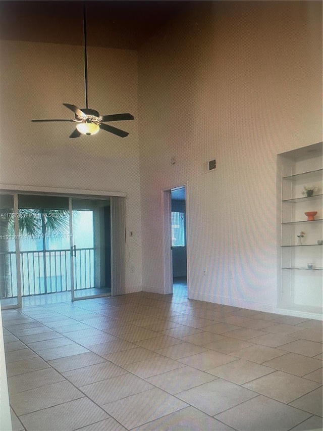 empty room with visible vents, wallpapered walls, ceiling fan, built in features, and a high ceiling