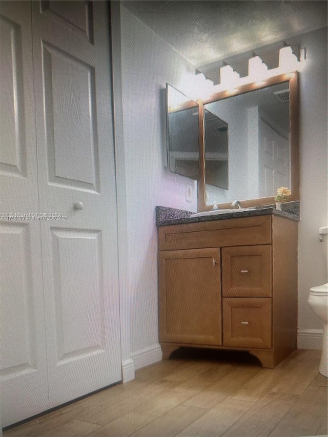 bathroom with toilet, wood finished floors, and vanity