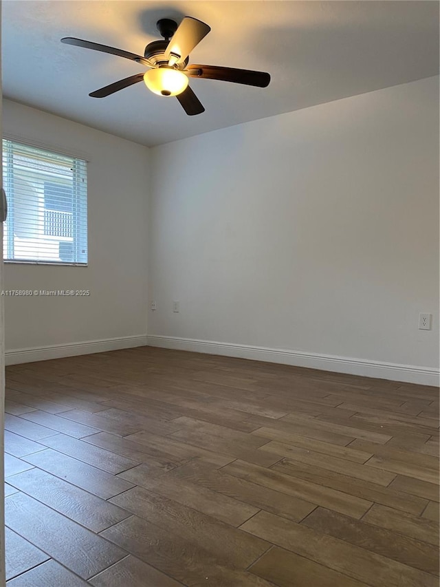 empty room with dark wood finished floors, ceiling fan, and baseboards