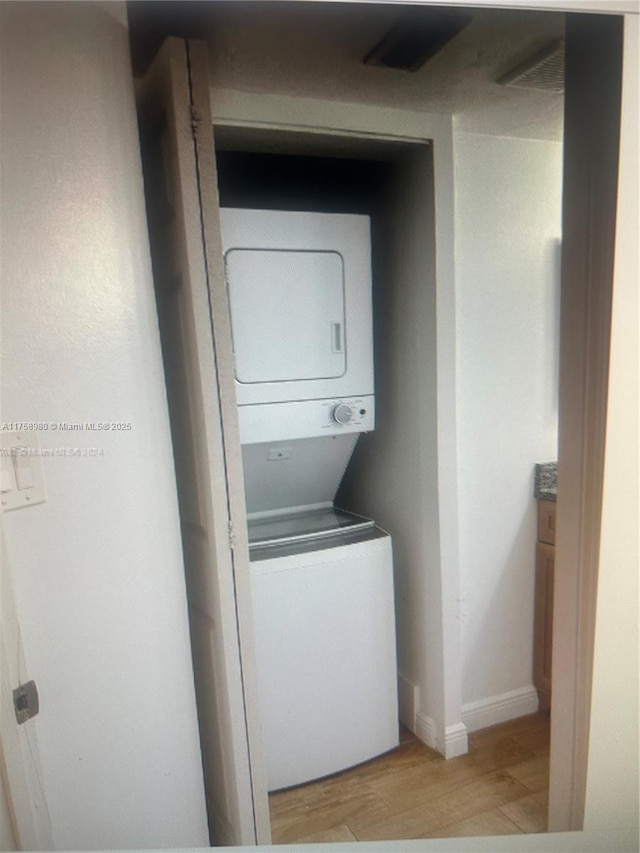 laundry room featuring light wood-type flooring, stacked washer / drying machine, and baseboards