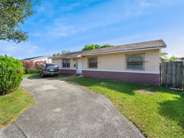 single story home with stucco siding, a front lawn, driveway, and fence