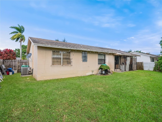 rear view of house featuring a yard, fence, cooling unit, and stucco siding