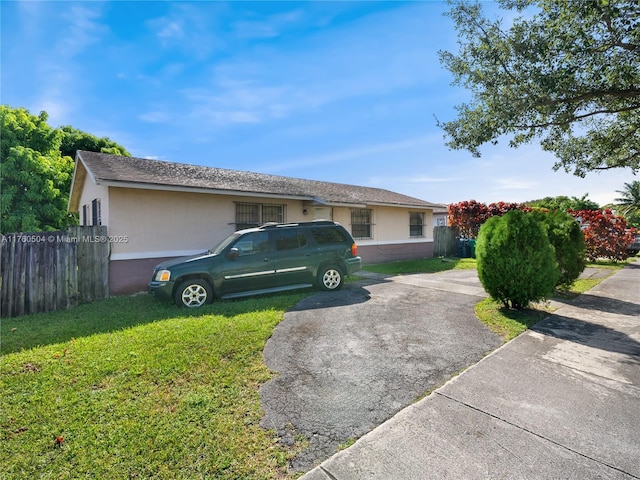 ranch-style house with stucco siding, driveway, a front lawn, and fence