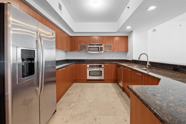 kitchen with visible vents, a sink, dark stone countertops, stainless steel appliances, and brown cabinetry