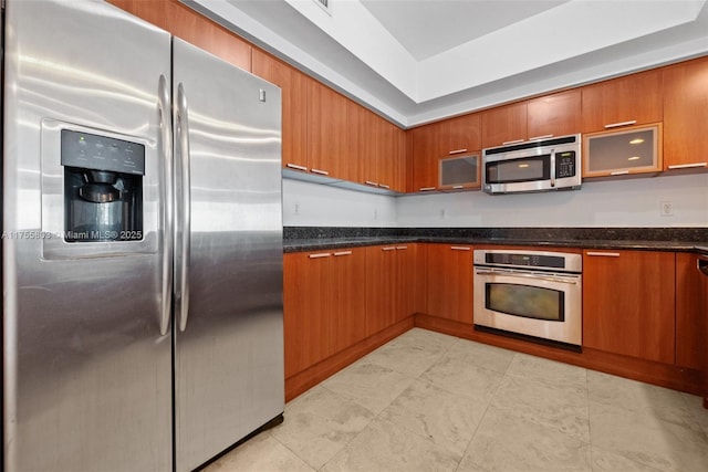 kitchen with dark stone counters, glass insert cabinets, brown cabinets, and stainless steel appliances