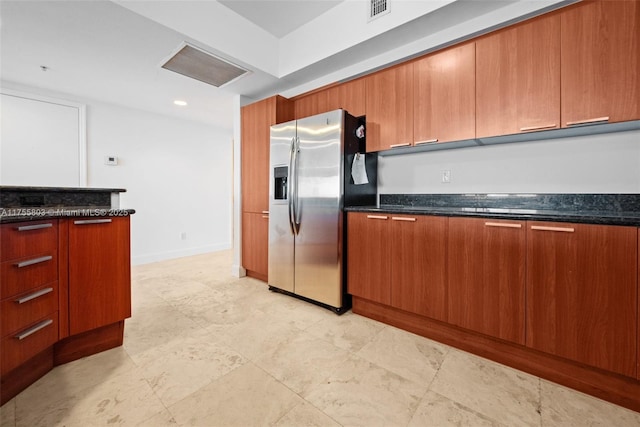 kitchen with brown cabinetry, visible vents, dark stone counters, and stainless steel refrigerator with ice dispenser