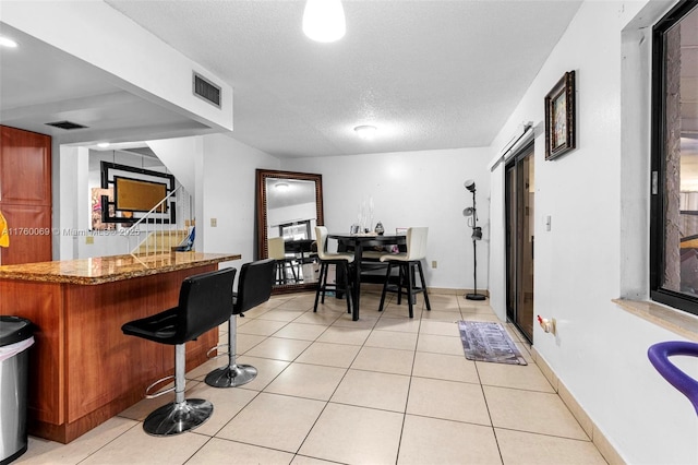 interior space featuring light tile patterned floors, visible vents, a textured ceiling, and a kitchen bar