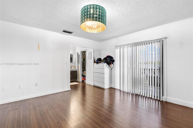 spare room with wood finished floors, baseboards, visible vents, an inviting chandelier, and a textured ceiling