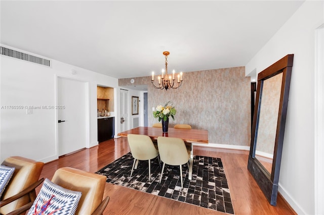 dining area featuring visible vents, wallpapered walls, baseboards, an inviting chandelier, and wood finished floors