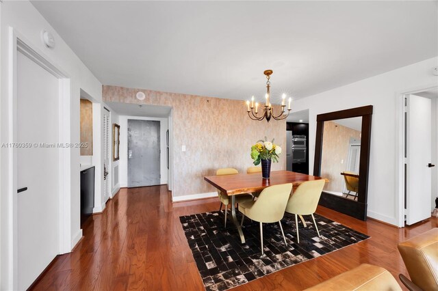 dining room with a notable chandelier, wallpapered walls, dark wood-type flooring, and baseboards