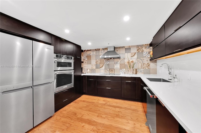 kitchen with light countertops, wall chimney exhaust hood, light wood finished floors, and a sink