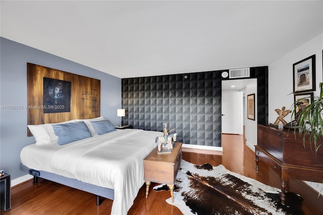 bedroom with an accent wall, wood finished floors, visible vents, and baseboards