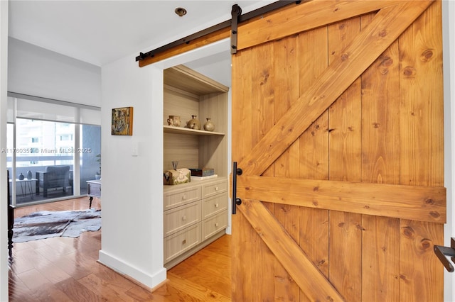 hall with a barn door, built in features, baseboards, and light wood finished floors