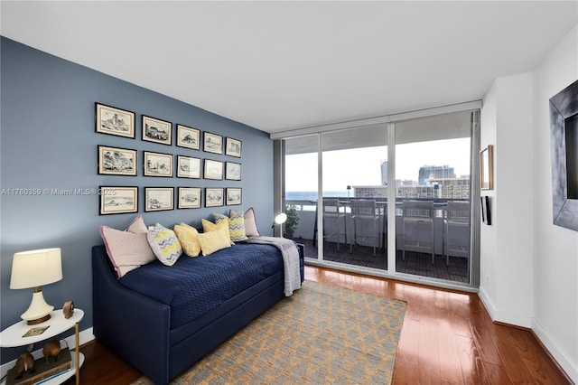 bedroom with access to outside, wood finished floors, baseboards, and expansive windows