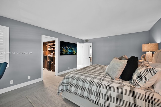 bedroom featuring visible vents, a walk in closet, baseboards, wood finished floors, and a closet