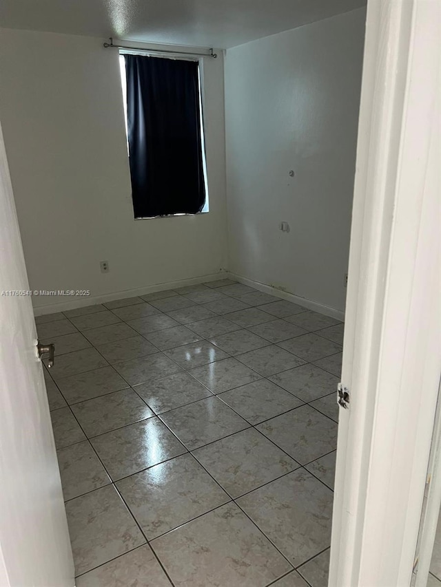 empty room with light tile patterned floors and baseboards