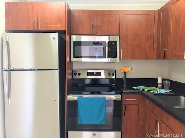 kitchen with a sink, dark stone counters, brown cabinets, and stainless steel appliances