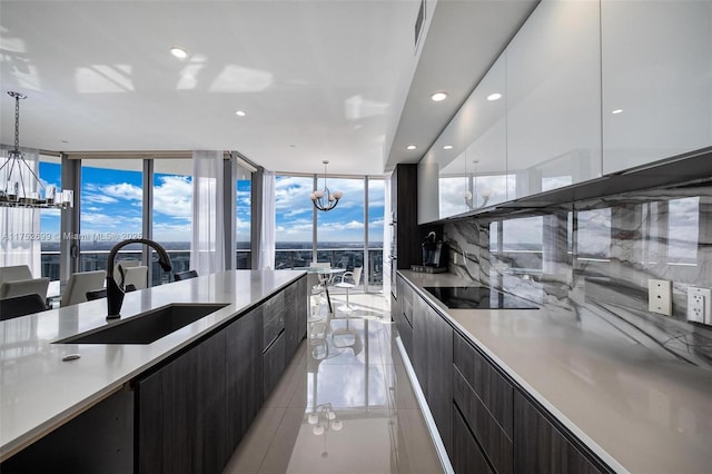 kitchen with black electric stovetop, a chandelier, light countertops, modern cabinets, and a sink