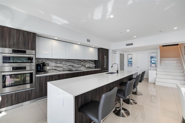 kitchen with backsplash, double oven, a breakfast bar, modern cabinets, and a sink