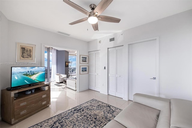 living area with light tile patterned floors, baseboards, visible vents, and ceiling fan